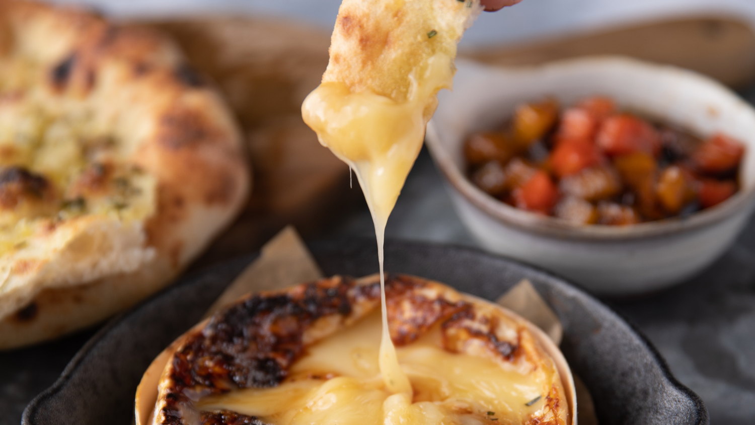 Baked Cheese being stretched out with jam and flatbreads in the background