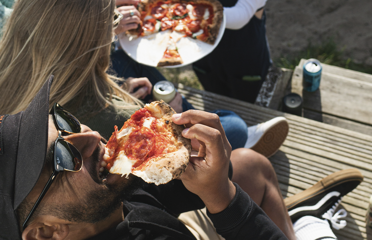 man taking bite of pizza slice outdoors