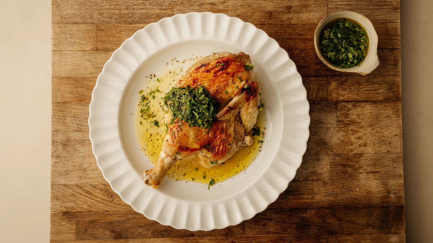 half chicken on a plate with a side of gremolata and on top of a cutting board.